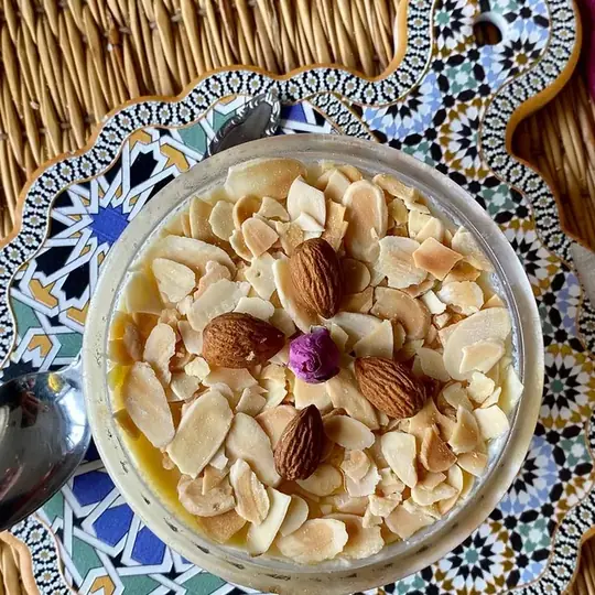 Crème d'amandes aux amandes effilées et bouton de rose, sur un dessous de plat en faïence.