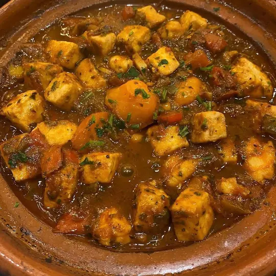 Tajine de poulet aux abricots et tomates, servi en cocotte de terre.