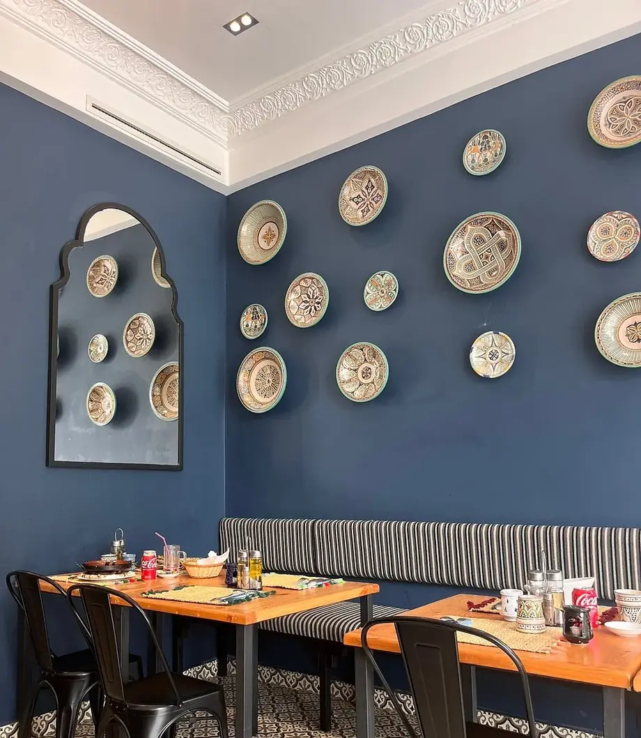 Collection d'assiettes en céramique de Safi accrochées sur le mur bleu, au-dessus d'une banquette rayée.